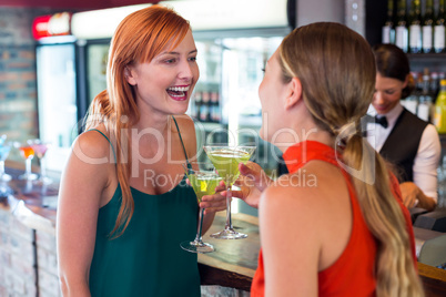 Happy friends holding a cocktail in front of bar counter