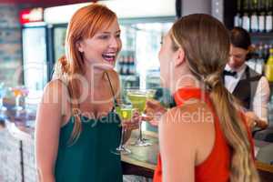 Happy friends holding a cocktail in front of bar counter