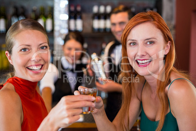 Portrait of happy friends holding a tequila shot in front of bar counter