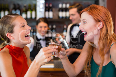 Happy friends holding a tequila shot in front of bar counter