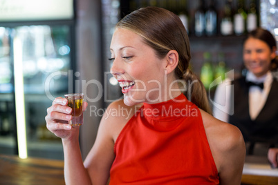 Happy woman holding a tequila shot in front of bar counter
