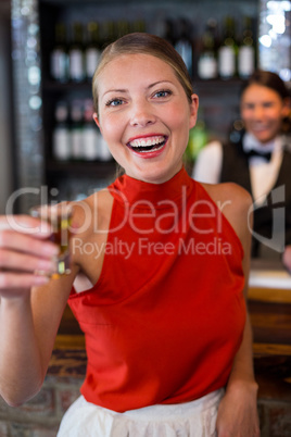 Portrait of happy woman holding a tequila shot in front of bar counter