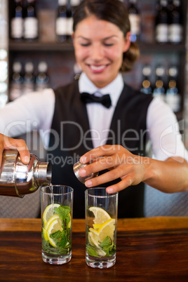 Bartender pouring a drink from a shaker to a glass on bar counter