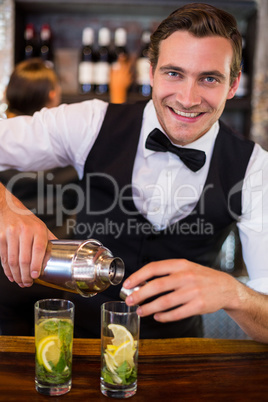 Portrait of bartender pouring a drink from a shaker to a glass on bar counter