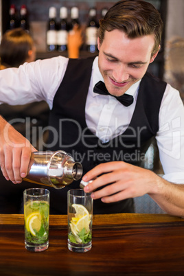 Bartender pouring a drink from a shaker to a glass on bar counter