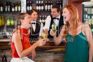 Happy friends holding a glass of gin in front of bar counter