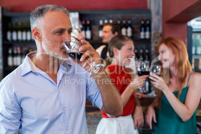 Man drinking red wine while two friends toasting the glasses in background