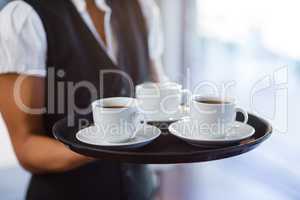 Mid section of waitress holding a tray of coffee cups