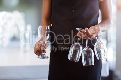 Mid section of waitress holding empty wine glasses