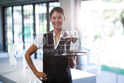 Smiling waitress holding a tray with glasses of red wine