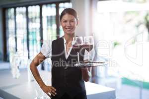 Smiling waitress holding a tray with glasses of red wine