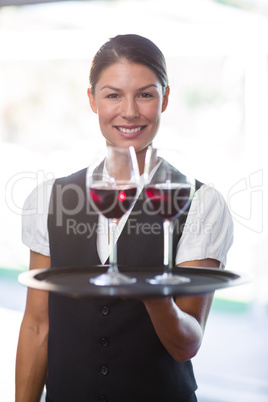 Smiling waitress holding a tray with glasses of red wine