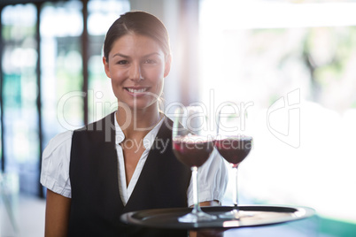 Smiling waitress holding a tray with glasses of red wine