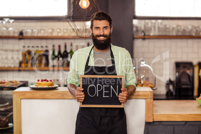 Portrait of a waiter holding a board written open