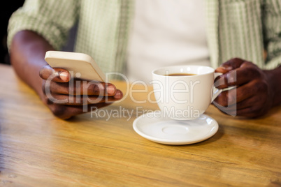 Hand holding a cup of coffee while using a smartphone