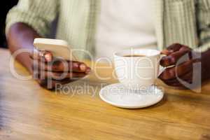 Hand holding a cup of coffee while using a smartphone