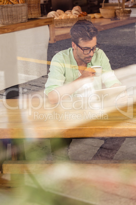 Hipster using a tablet computer while drinking a cup of coffee