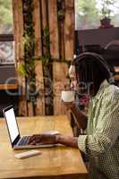 Hipster drinking a cup of coffee while using a laptop