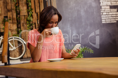 Woman drinking coffee and using smartphone