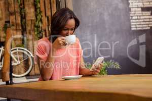 Woman drinking coffee and using smartphone