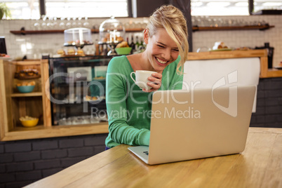 Woman drinking coffee and using laptop