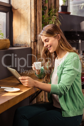 Smiling woman drinking coffee and using tablet