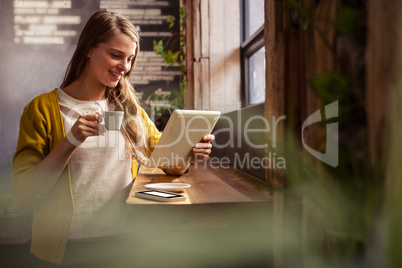 Smiling woman drinking coffee and using tablet