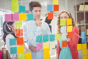 Casual colleagues looking at sticky notes on wall