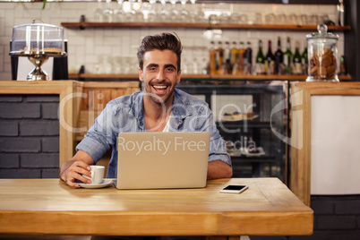 Hipster man smiling at camera while using laptop