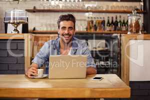 Hipster man smiling at camera while using laptop