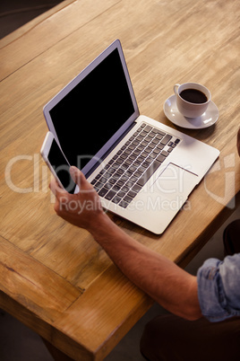 Cropped image of laptop and man using smartphone
