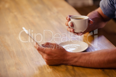 Cropped image of hipster man using smartphone while drinking cup of coffee