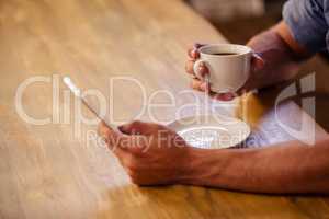 Cropped image of hipster man using smartphone while drinking cup of coffee