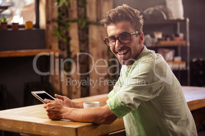 Happy hipster man posing for camera while using tablet