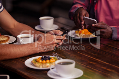 Cropped image of friends eating pastries and drinking coffee
