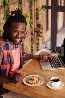 Smiling hipster man posing with pastry and laptop