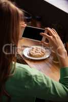 Over the shoulder view of hipster woman taking picture of pastry