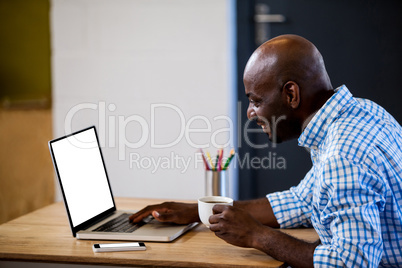 Profile view of businessman holding a coffee and typing on his laptop