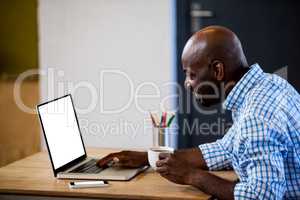 Profile view of businessman holding a coffee and typing on his laptop