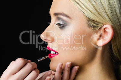 Blonde woman having her lips made up by makeup artist