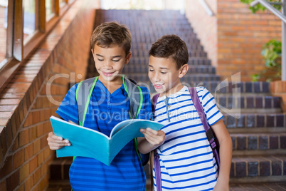 Smiling school kids reading a book on staircase