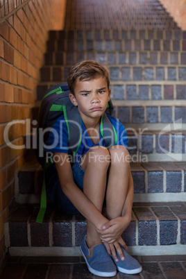 Sad schoolboy sitting alone on staircase