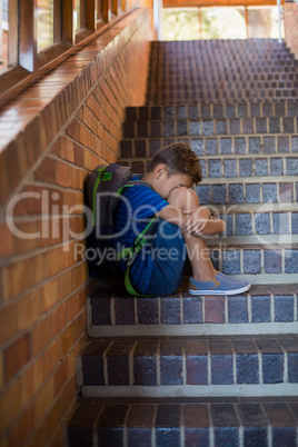 Sad schoolboy sitting alone on staircase