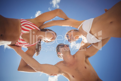 Friends forming huddle against sky