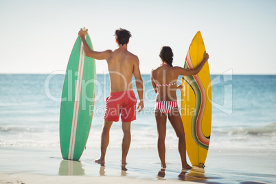Couple standing with surfboard on beach