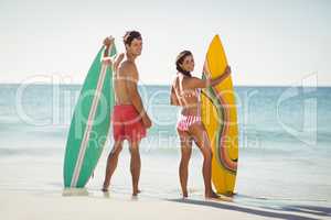 Couple standing with surfboard on beach