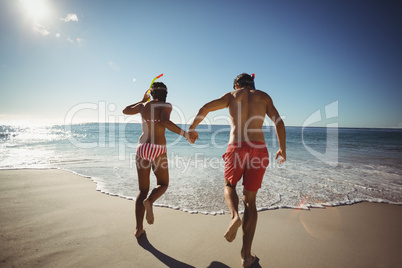 Couple wearing diving mask running on beach