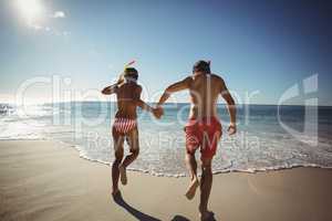 Couple wearing diving mask running on beach