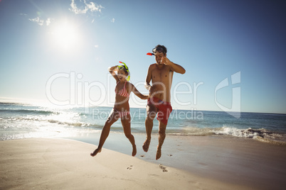Couple wearing diving mask jumping on beach