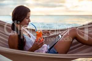 Woman using digital tablet and having mocktail on a hammock